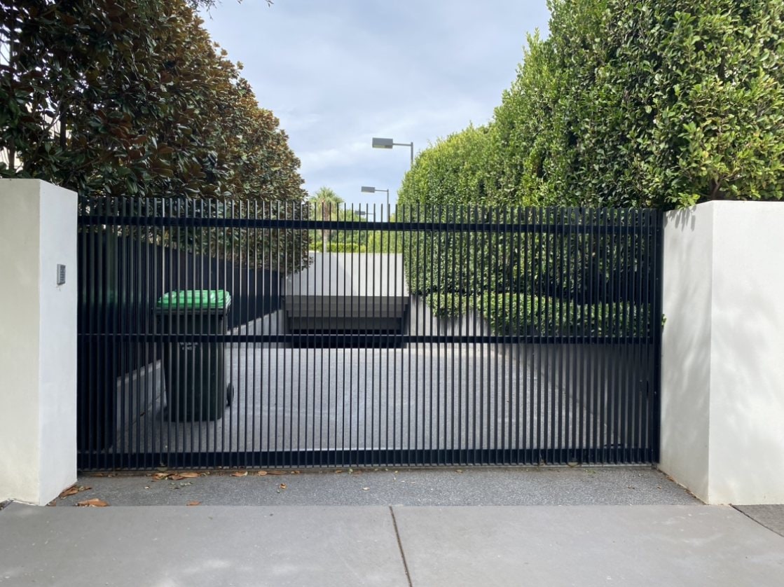 Black horizontal bar sliding gate between white piers