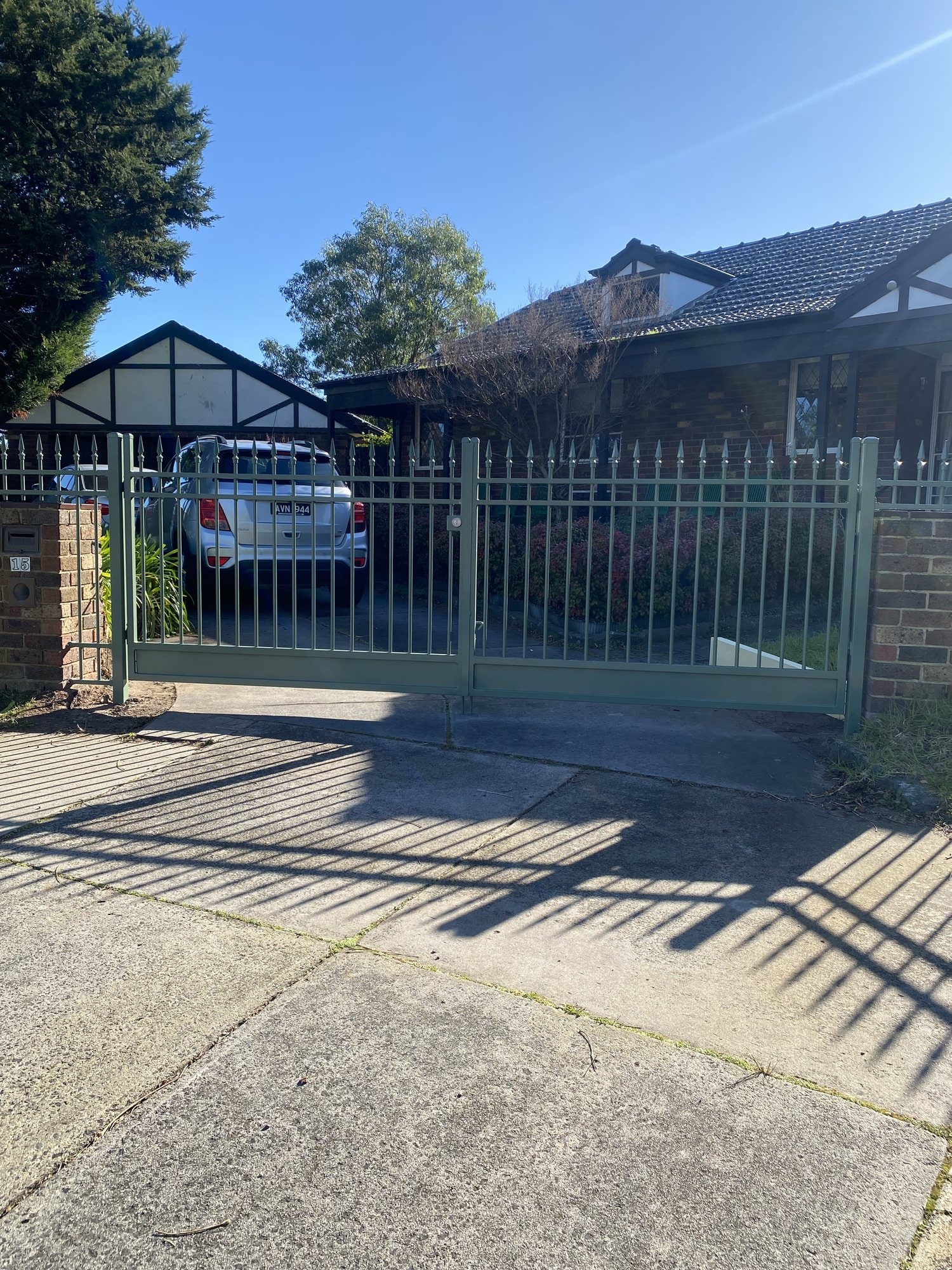 Sage green palisade driveway gate between brick piers