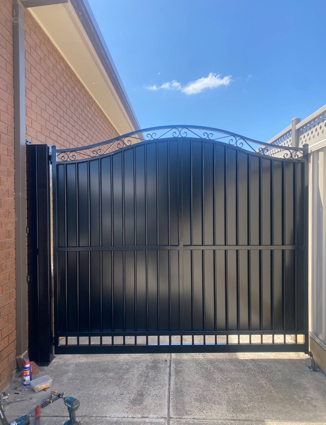 Arched black privacy driveway gate with scroll top
